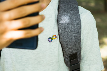 Teenage boy with autism infinity rainbow symbol sign using smartphone outdoors. World autism awareness day, autism rights movement, neurodiversity, autistic acceptance movementの写真素材