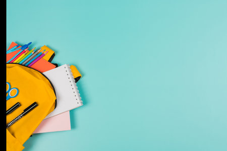 Back to school, education, learning concept. Open yellow backpack with school supplies on pastel blue background. Top view, copy spaceの写真素材