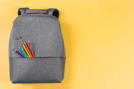 Gray backpack with autism infinity rainbow symbol sign, colored pencils in yellow background. Top view. World autism awareness day, autism rights movement, neurodiversity, autistic acceptance movementの写真素材