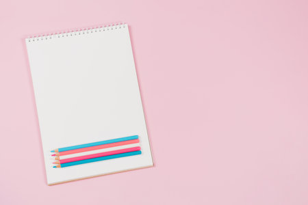 Open white notebook with light blue, pink, white colored pencils on pastel pink background. Top view, copy space for textの写真素材