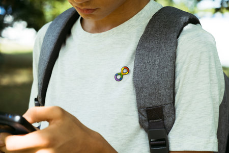 Teenage boy with autism infinity rainbow symbol sign using smartphone outdoors. World autism awareness day, autism rights movement, neurodiversity, autistic acceptance movementの写真素材