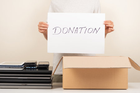 Donate technology to charity. Old used laptop computers, phone, tablet near cardboard box. Volunteer...