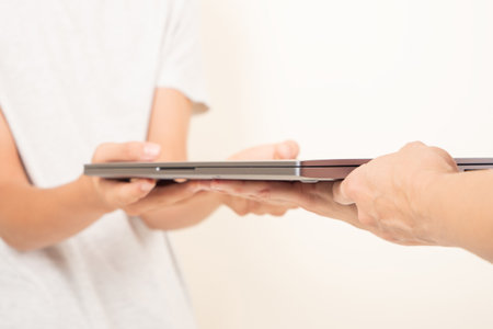 One person hands holding old laptop computer and give it to another person. Donation, charity, e-waste, remote learning, online working, electronic waste for reuse, refurbish, repair, recycle conceptの写真素材