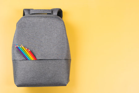 Gray backpack with colored pencils in rainbow colors on yellow background. Top view, copy space. Back to school, education, learning conceptの写真素材