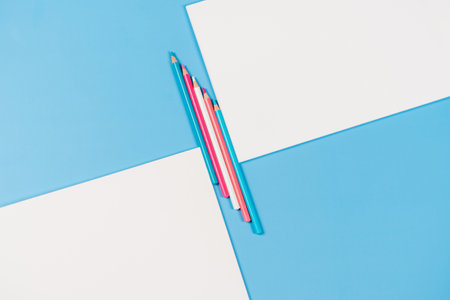 Two white notebooks with light blue, pink, white colored pencils between on light blue background. Top view, copy space for textの写真素材