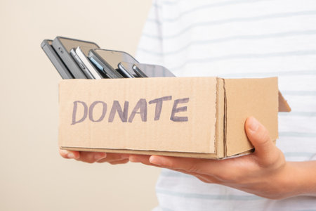 Donations of used cell phones. Volunteer hands holding cardboard box full of old used smartphones. Donation, e-waste, electronic waste charityの写真素材