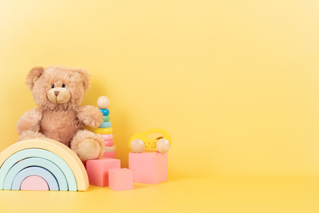 Educational kids toys collection. Teddy bear, wooden rainbow pink cubes and colorful balls on yellow background. Front viewの写真素材