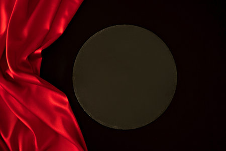 Empty round black platform podium stand on red and black silk satin background. Mockup podium for cosmetic product presentation. Top viewの写真素材