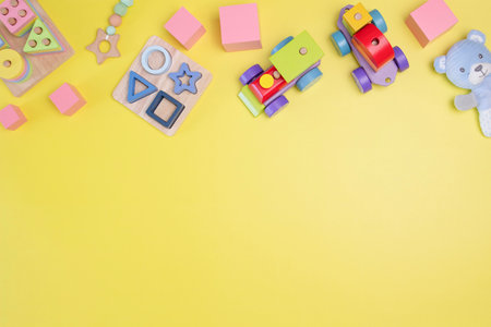 Toys on yellow background. Natural wooden educational toys including stacking shape sorter, colorful train, building blocks, sensory toys for children. Top view, flat lay frameの写真素材