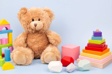 Kid toys background. Cute plush teddy bear and Montessori wooden educational toys for children on light blue background. Front viewの写真素材