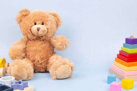Kid toys background. Cute plush teddy bear and wooden educational toys for children on light blue...