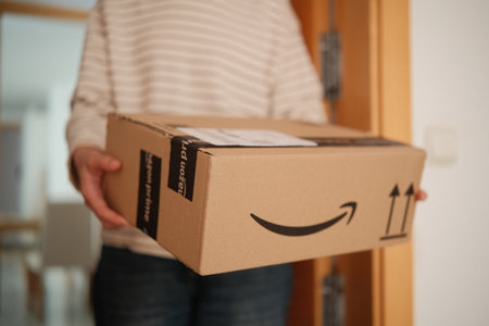 Alicante, Spain - February 02, 2026: Receiving Amazon online Order at home. Amazon prime delivery. Woman holding cardboard box with Amazon prime logo at home entranceのeditorial素材