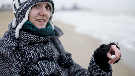 Smiling girl hold little white seashell on the beach in winterの写真素材