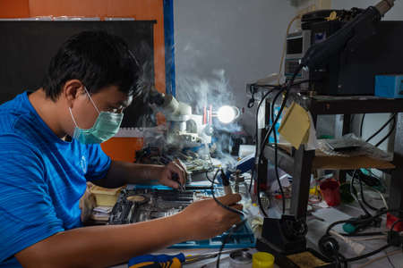 Repairman is using a hot solder to fix a computer motherboard.