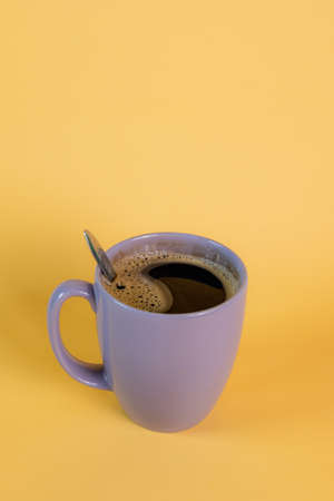 Purple mug with hot black coffee with a few bubbles on a yellow background, taken in a studio.の写真素材