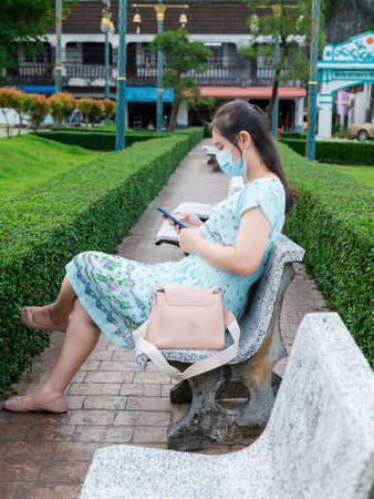 An Asian woman reading long-recorded messages on her mobile phone reminds me of the past. In the park wearing a mask to protect it for safety.の写真素材