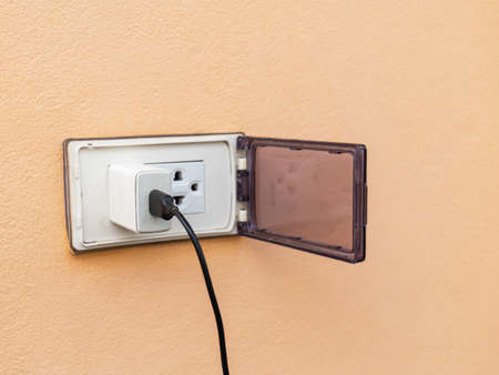 old white adapter There is a charging cable plugged in. With outdoor wall plugs, there is a cover that closes when not in use to prevent danger. There is a coppy space.の写真素材