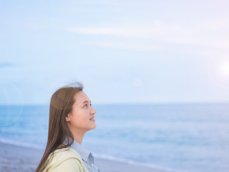 Take a shot at the head of an Asian woman walking by the sea. along the beach looking at the sky free sample release The wind blows, there is a flare.の写真素材