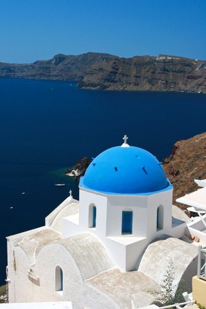 A classic image of Santorini, one of the most spectacular of all of the Greek Islands. White wash walls, blue roof church and blue sky beside the Agean sea.の写真素材