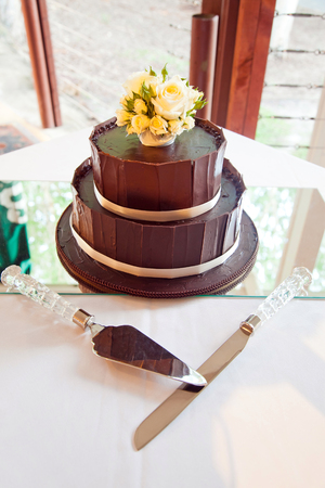 Chocolate layered wedding cake with rose flowers and silver serving utensilsの写真素材