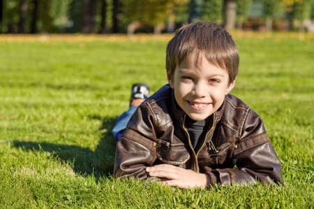 Little 7 year boy Lying Down on the green grass and smilingの写真素材