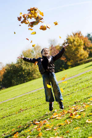 little 7 year boy throwing up yellow autumn  leafes in the parkの写真素材