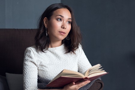 a young,beautiful girl wrapped in a warm plaid blanket reading a book. studio shootの写真素材