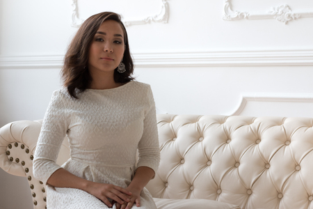 Pretty girl in white dress sits on a White Leather couch. Super model.の写真素材