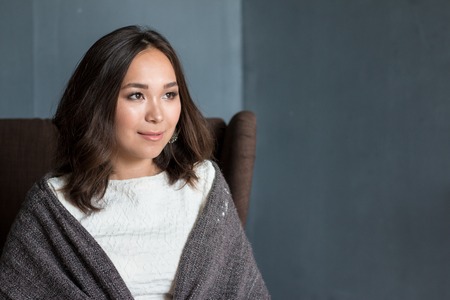 Beautiful woman in the room wrapped in a plaid blanket sitting in armchair dreaming and planning her autumn vacation. 2016の写真素材