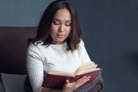 a young,beautiful girl wrapped in a warm plaid blanket reading a book. studio shootの写真素材