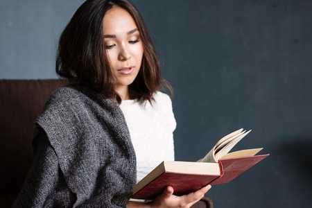 a young,beautiful girl wrapped in a warm plaid blanket reading a book. studio shootの写真素材