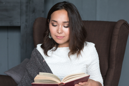 a young,beautiful girl wrapped in a warm plaid blanket reading a book. studio shootの写真素材