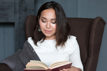 a young,beautiful girl wrapped in a warm plaid blanket reading a book. studio shootの写真素材