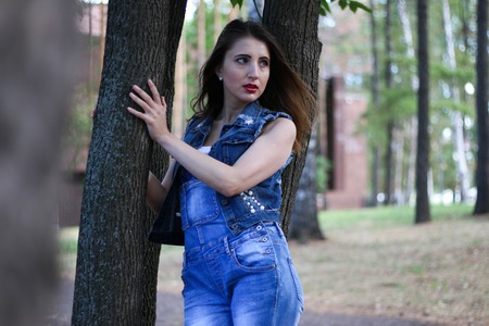 Woman in overalls stands between tree trunksの写真素材