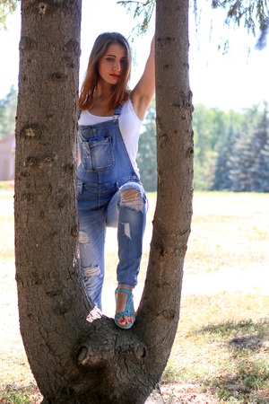 Woman in overalls stands between tree trunksの写真素材