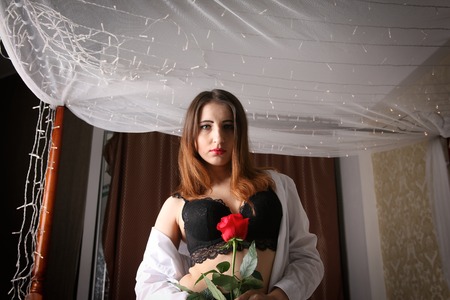 Sexy woman wearing a white mens shirt and black bra ad panties sits on bedの写真素材