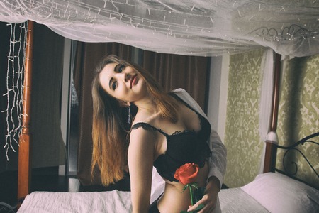 Sexy woman wearing a white mens shirt and black bra ad panties sits on bedの写真素材