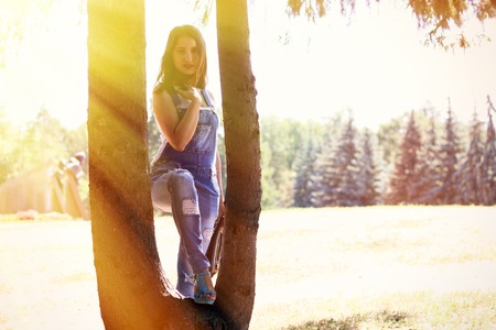 Woman in overalls stands between tree trunksの写真素材