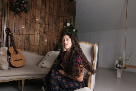 Young Hispanic woman sitting in chair in the Christmas interior and waiting for celebrationの写真素材