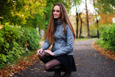 The girl squats in autumn wood in shining sun beamsの写真素材