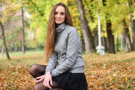 The girl squats in autumn wood in shining sun beamsの写真素材