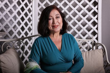 Mature Asian woman sitting on couch in luxurious dressの写真素材