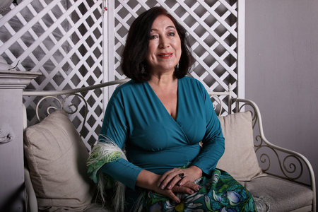 Mature Asian woman sitting on couch in luxurious dressの写真素材