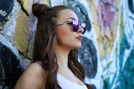 Beautiful girl dressed in a street style outfits posing in front of wall full of graffitis.の写真素材