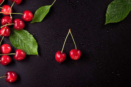 Red cherries on black background. Couple of cherries in the middle. Tasty fruit. Top view.