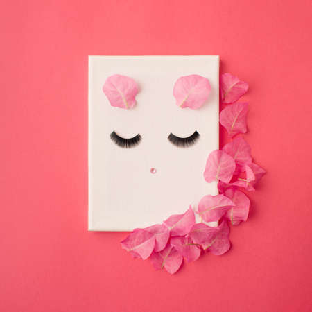 Cute  abstract face on white canvas with flower petals on pink background
