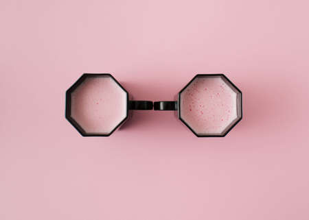 Two black cups with pink beverage on pink background. Flat layの写真素材