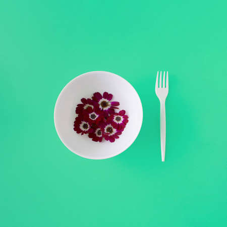 Bowl with purple flowers and white fork on turquoise background. Flat lay.