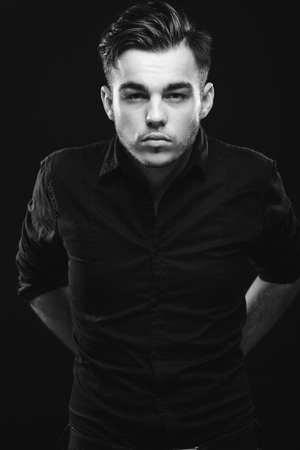 Confident man with beard and dark hair, wearing in black shirt, is posing on black background and looking at camera, waist upの写真素材