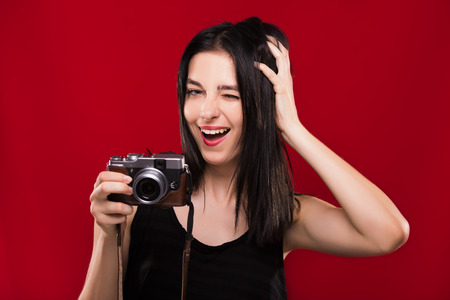 Young cheerful woman, with dark hair, wearing on black blouse, posing with camera and having fun, on the red background, waist upの写真素材